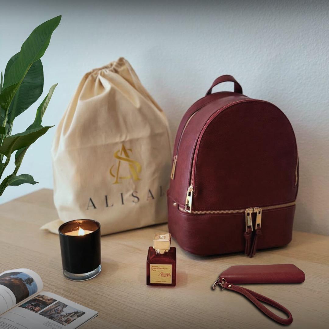 Burgundy backpack, pouch, and candle on a wooden surface with 'ALISAR' branded bag in the background.