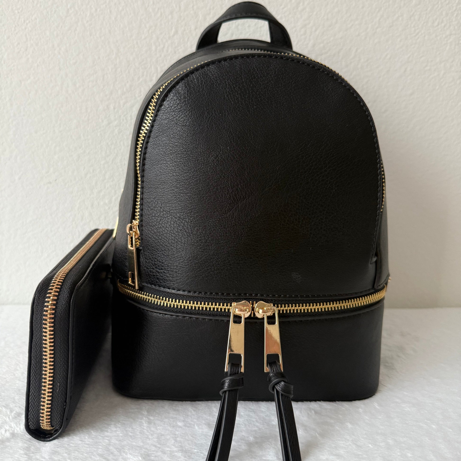 Black backpack with gold zippers on a textured white surface