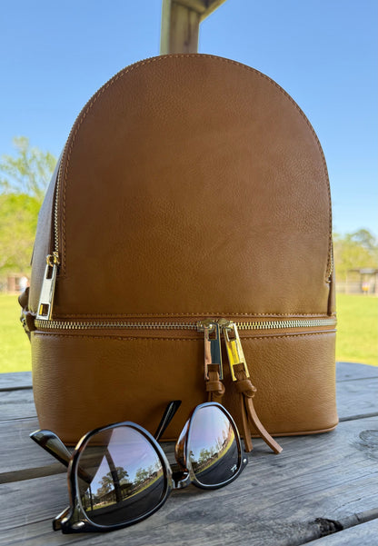 Mustard leather backpack with sunglasses on a wooden surface outdoors