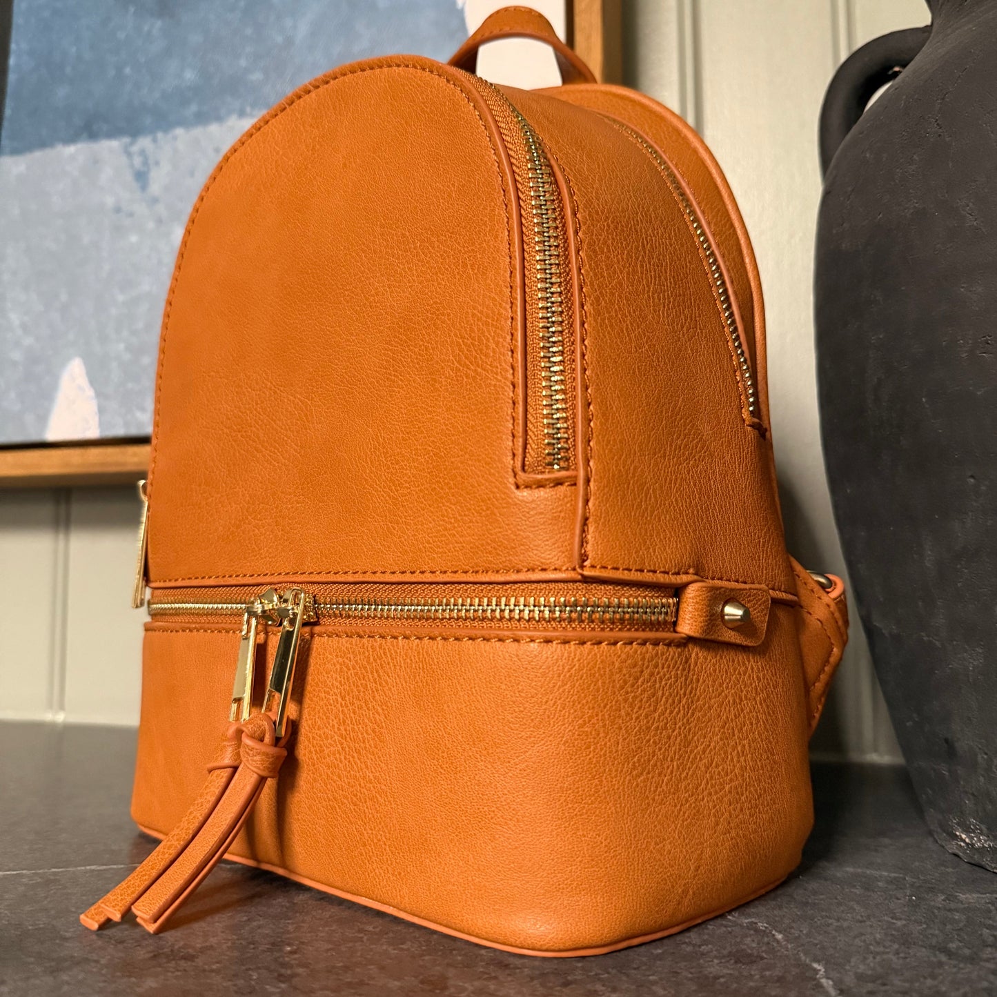Tan  leather backpack with gold zipper on a textured surface