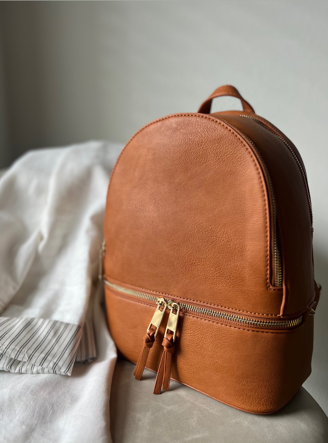 Tan leather backpack on a light gray surface with a neutral background