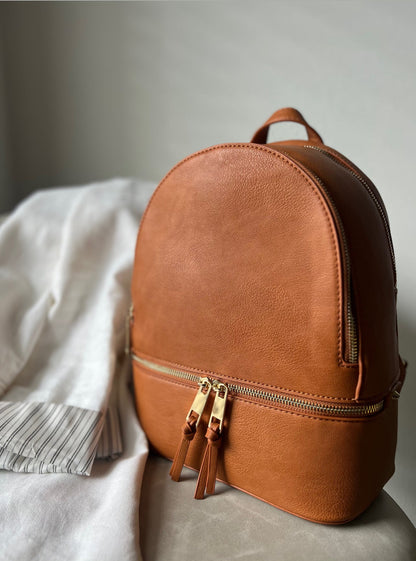 Tan leather backpack on a light gray surface with a neutral background